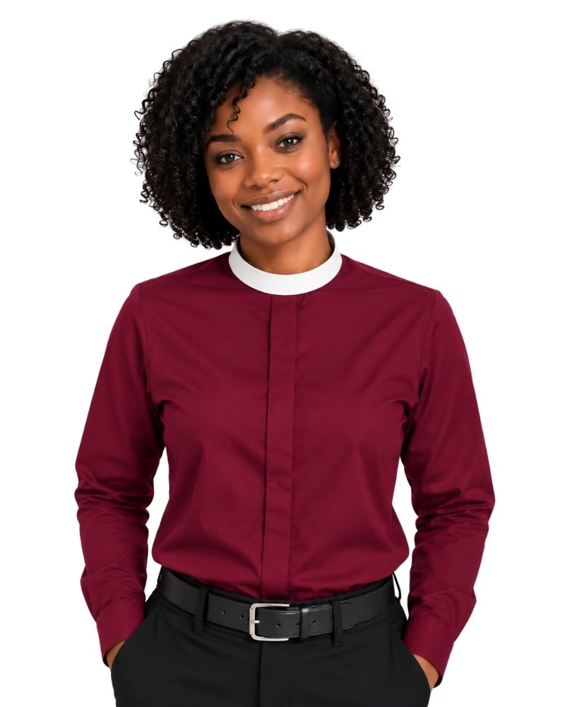 A smiling woman with curly black hair wearing a long-sleeve burgundy clerical shirt with a contrasting white crew neck collar, paired with black trousers and a black belt, against a plain white background.