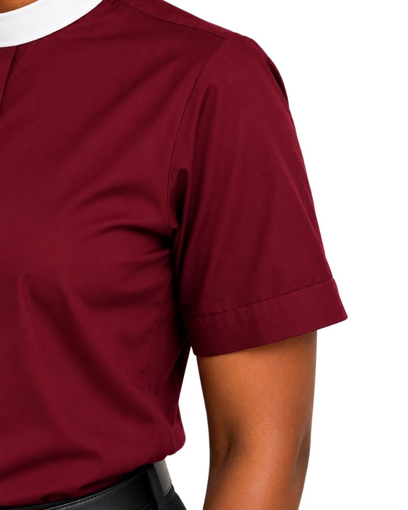 Close-up of a woman wearing a short-sleeve clerical shirt in deep burgundy with a white collar trim, shown against a plain white background.