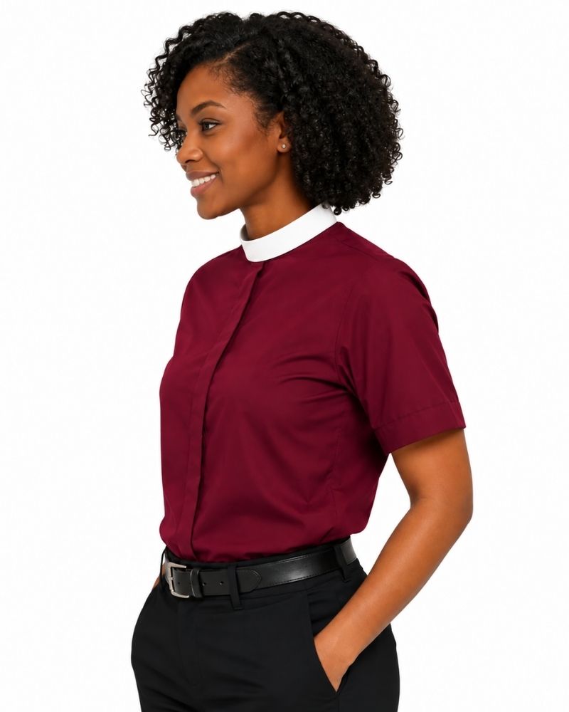 A woman wearing a short-sleeve burgundy clerical shirt with a contrasting white collar, paired with black trousers and a black belt, shown in a side-profile view against a plain white background.