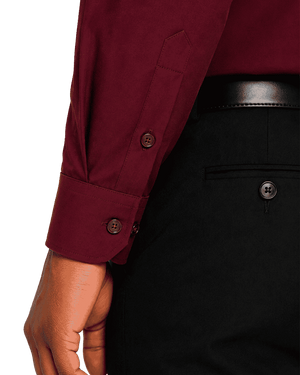 Close-up of a person wearing a burgundy long-sleeve clerical shirt with a buttoned cuff, paired with black trousers and a black belt.