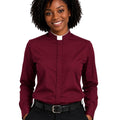 A smiling woman with curly black hair wearing a burgundy long-sleeve clerical shirt with a white collar, paired with black trousers and a black belt, against a plain white background.