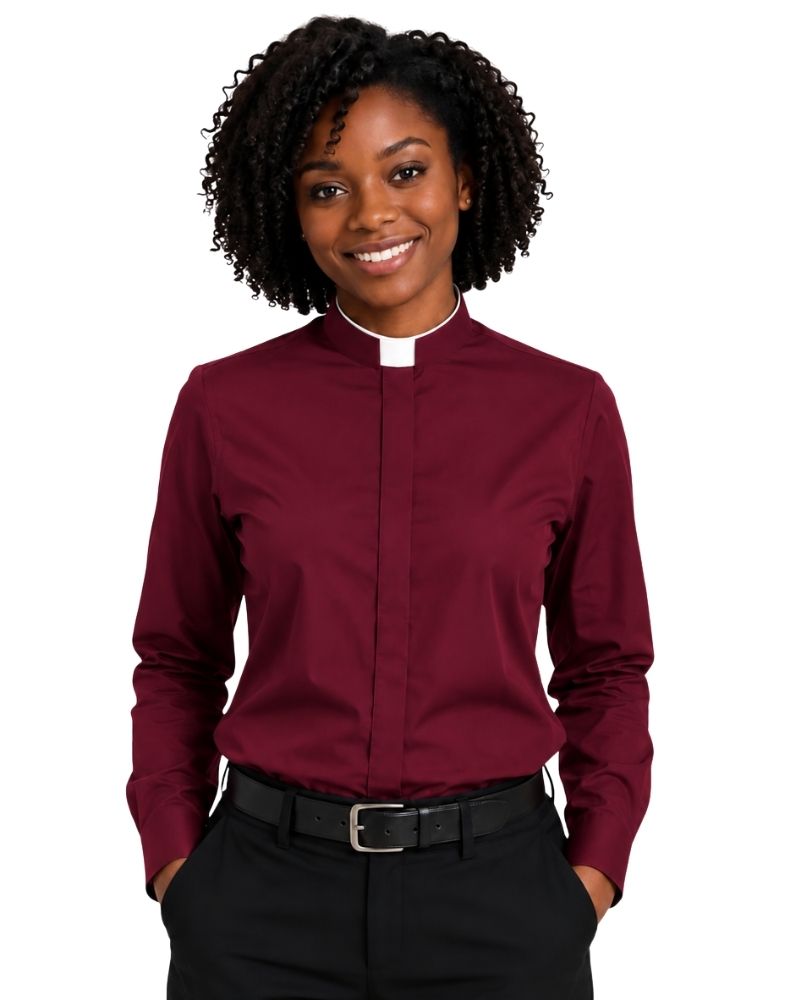 A smiling woman with curly black hair wearing a burgundy long-sleeve clerical shirt with a white collar, paired with black trousers and a black belt, against a plain white background.
