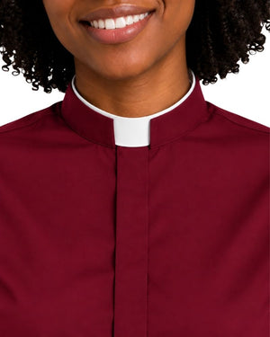 A close-up of a woman wearing a burgundy clerical shirt with a white collar tab, shown from the chest up against a plain white background.