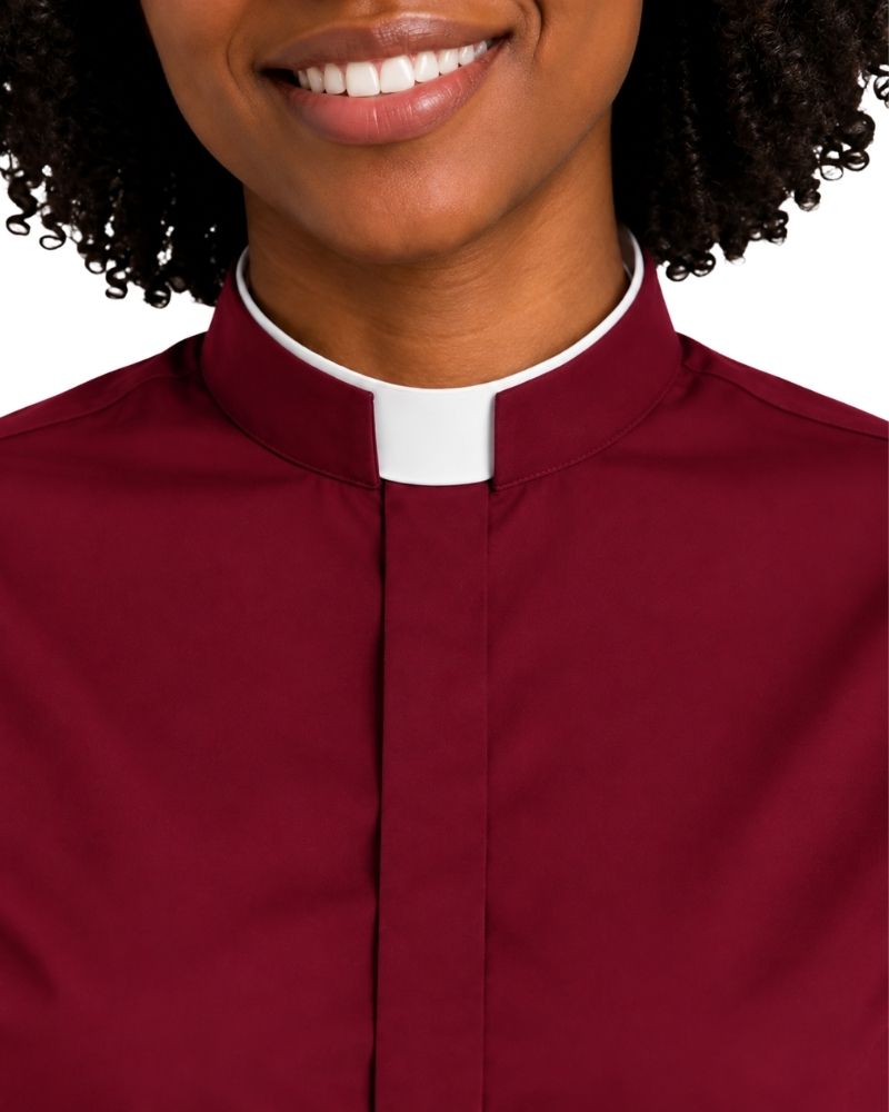 A close-up of a woman wearing a burgundy clerical shirt with a white collar tab, shown from the chest up against a plain white background.