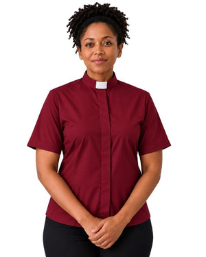 A smiling woman with curly black hair wearing a short-sleeve burgundy clerical shirt with a white collar, paired with black trousers and a black belt, against a plain white background.