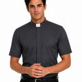A man wearing a dark gray short-sleeve clerical shirt with a white collar tab, paired with black trousers and a black belt, against a plain white background.