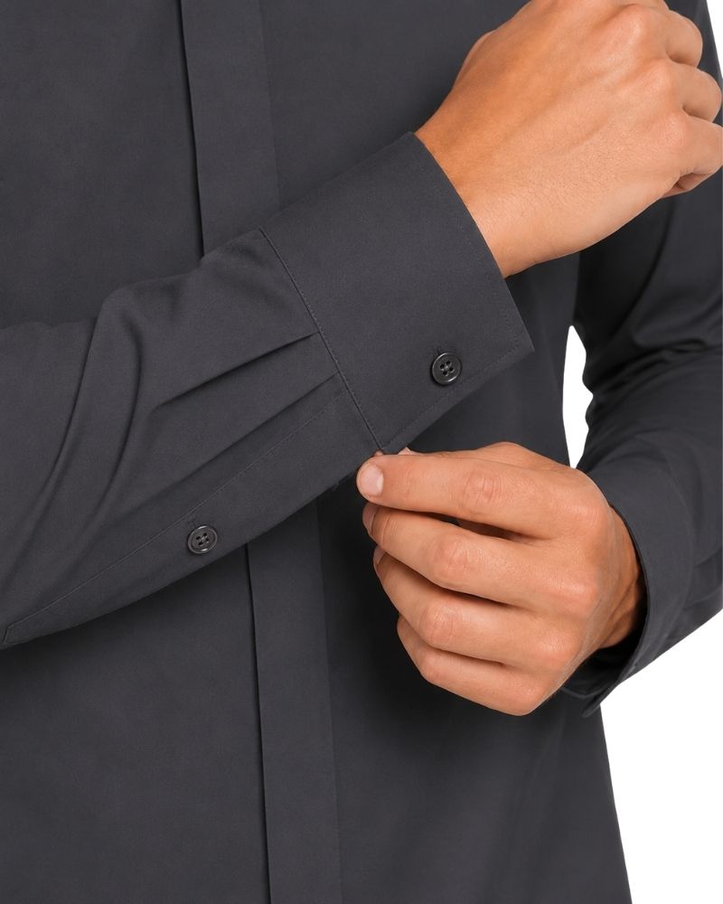 Close-up of a man's hands cuffing a dark charcoal gray long-sleeve clerical shirt.