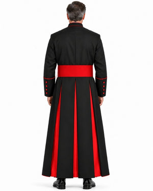 A man viewed from the back wearing a Classic Black Clergy Cassock with Red Trim with a wide red waist sash and red vertical panels on the skirt, against a plain white studio background.