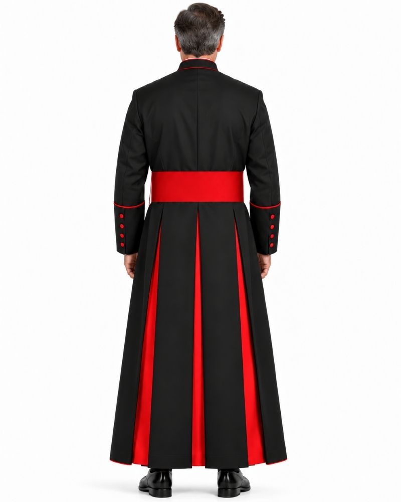 A man viewed from the back wearing a Classic Black Clergy Cassock with Red Trim with a wide red waist sash and red vertical panels on the skirt, against a plain white studio background.