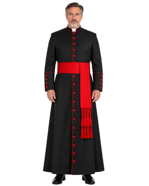 A man modeling a Classic Black Clergy Cassock with Red Trim a wide red waist sash and a matching red draped scarf with tassels, set against a plain white background.