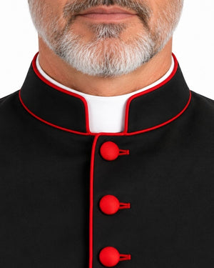 Close-up of a man wearing a Classic Black Clergy Cassock with Red Trim with red piping and red buttons over a white collar, against a plain white background.