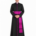 A man wearing a Classic Clergy Cassock With Magenta Trim, a matching magenta sash, and magenta buttons, standing against a plain white studio background.