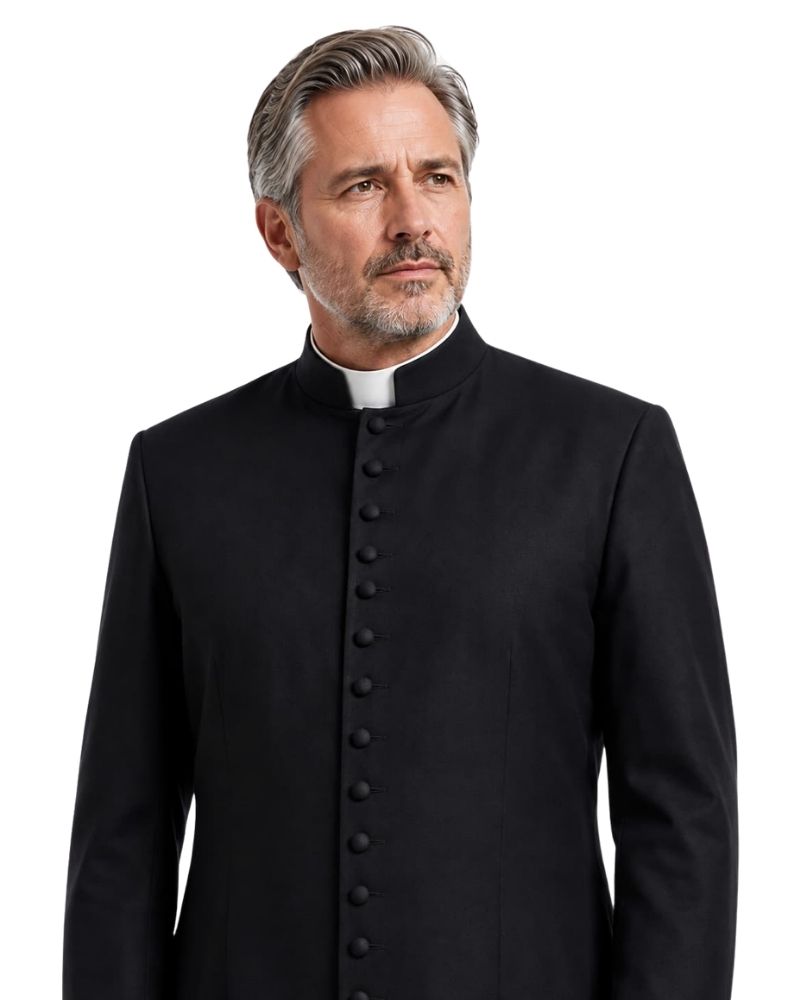 A man with gray hair and a beard wearing a black clerical-style Cassock over a white collar, photographed against a plain white background.