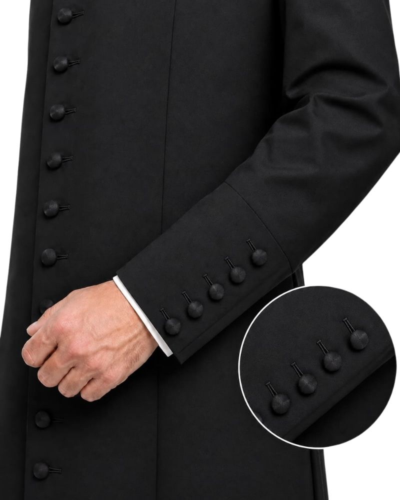 Close-up of a black long Cassock with a double-breasted front, buttoned cuffs, and a white shirt cuff visible at the wrist, worn by a model.