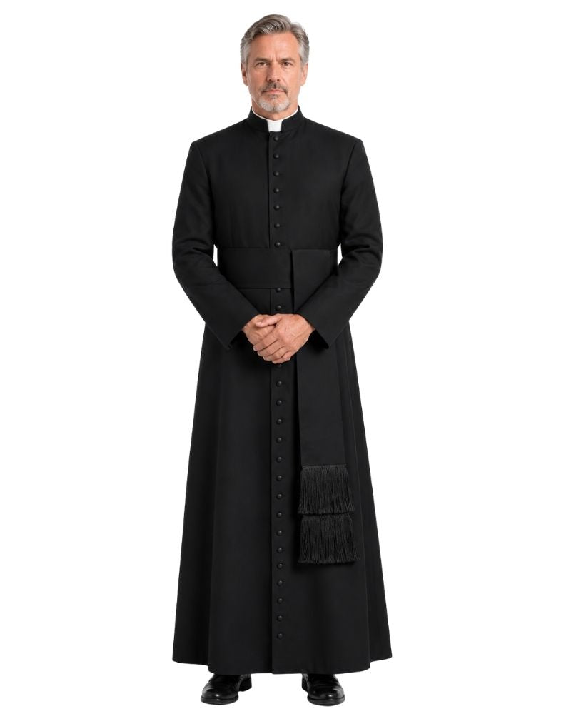 A man modeling a long black clerical robe costume with a high collar, front button closure, and a decorative black fringed pocket, set against a plain white background.
