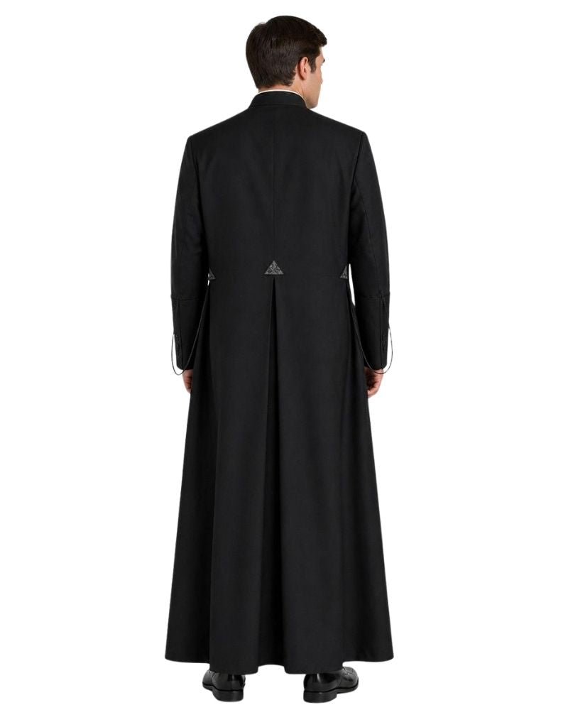 A man viewed from the back wearing a long black cassock over a dark robe, standing against a plain white background.