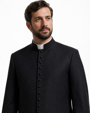 A man wearing a black clerical cassock with a high stand-up collar and a white clerical collar, photographed against a plain white background.