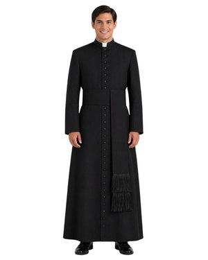 A man wearing a long black clerical cassock with a high collar, front button closure, waist tie, and a matching black scapular with fringe, photographed against a plain white background.
