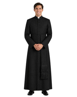 A man modeling a long black clerical cassock with a high collar, front buttons, and a small white clerical collar, photographed against a plain white background.