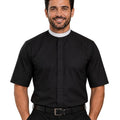 A smiling man wearing a black short-sleeve clerical shirt with a white collar, paired with black trousers and a black belt, against a plain white background.