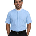 A smiling man wearing a light blue short-sleeve clerical shirt with a white collar, paired with black trousers and a black belt, against a plain white background.