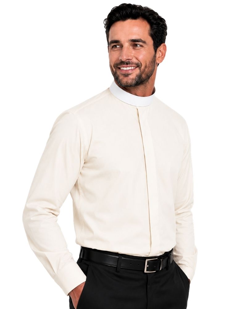 A smiling man wearing a cream-colored long-sleeve clerical shirt with a high mock neck and front pleat detail, paired with black trousers and a black belt, against a plain white background.