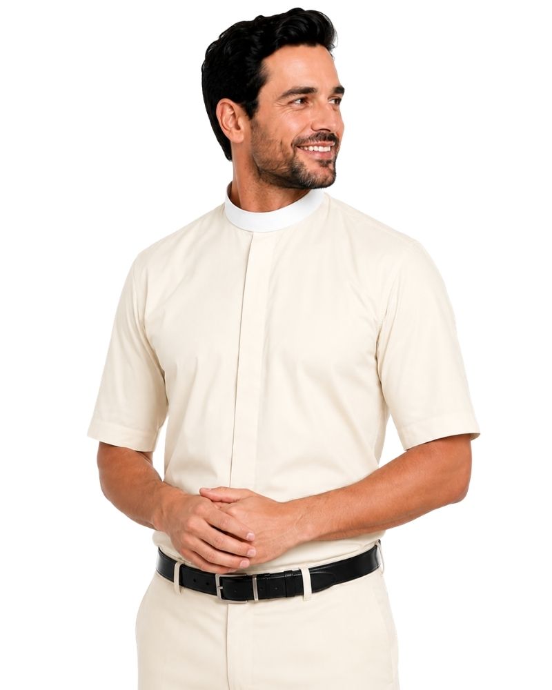 A man wearing a short-sleeve cream-colored priest clerical shirt with a white mock neck collar, paired with cream trousers and a black belt, against a plain white background.