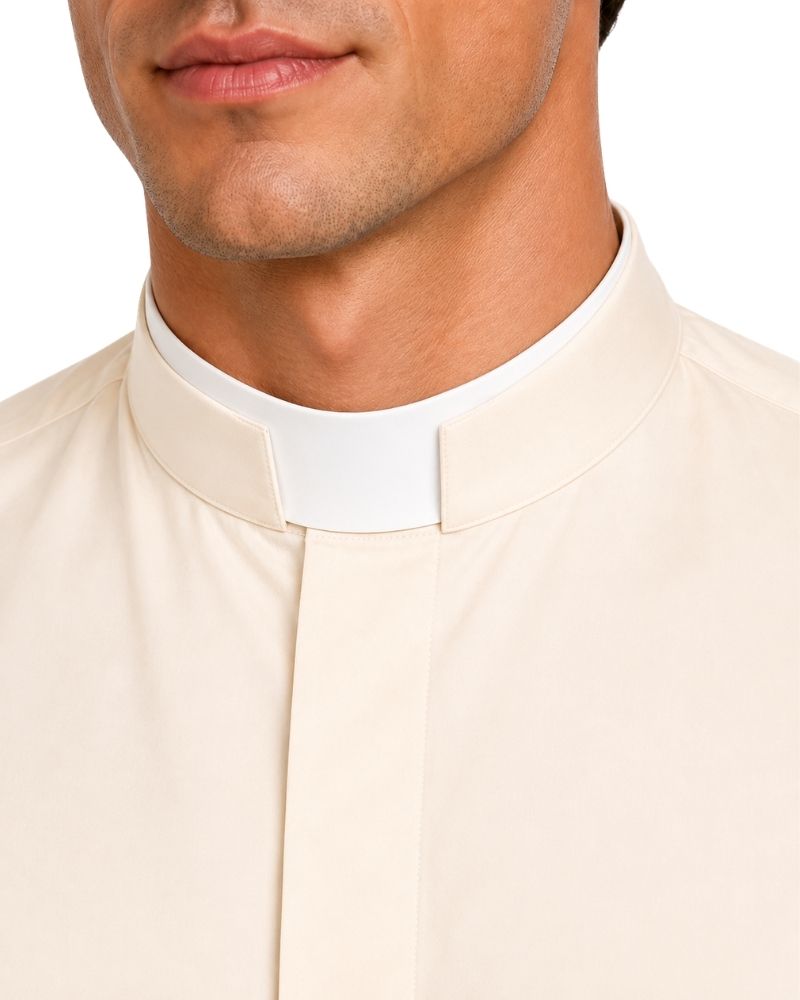 Close-up of a man wearing a cream-colored clerical shirt with a white collar, set against a plain white background.