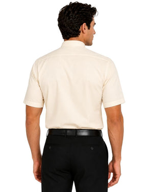 A man viewed from the back wearing a short-sleeve cream-colored clerical shirt and black trousers, set against a plain white background.