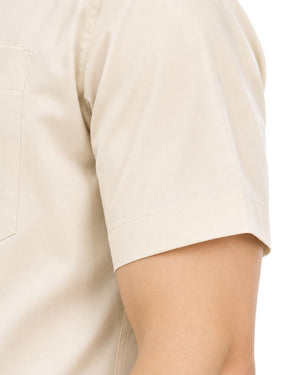 Close-up of a man wearing a short-sleeve beige clerical shirt showing the sleeve, chest pocket, and part of the arm against a white background.