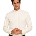 A man wearing a cream-colored long-sleeve clerical shirt with a high mock neck and white collar, paired with black trousers and a black belt, against a plain white background.