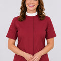 Woman wearing a maroon clerical shirt with a white collar against a plain background