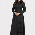 Woman wearing a long black coat with a sash on a white background