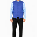 Man wearing a blue vest over a light blue shirt with black pants on a white background