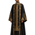 A man modeling a long black liturgical robe with ornate gold embroidery, a white collar, and a gold cross pendant, photographed against a plain white background.