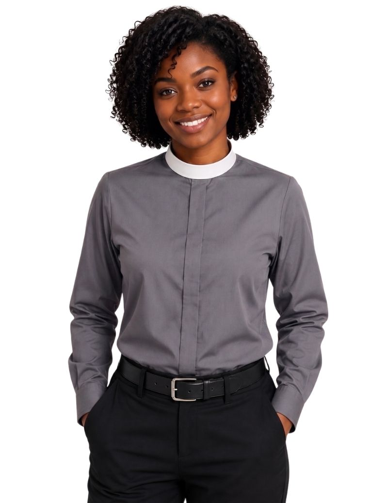 A smiling woman with curly black hair wearing a gray long-sleeve clerical shirt with a white mock neck collar, paired with black pants and a black belt, against a plain white background.