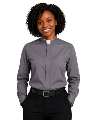 A smiling woman with curly black hair wearing a long-sleeve gray clerical shirt with a white collar, paired with black trousers and a black belt, against a plain white background.