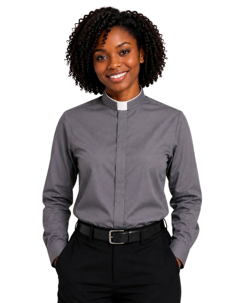 A smiling woman with curly black hair wearing a long-sleeve gray clerical shirt with a white collar, paired with black trousers and a black belt, against a plain white background.