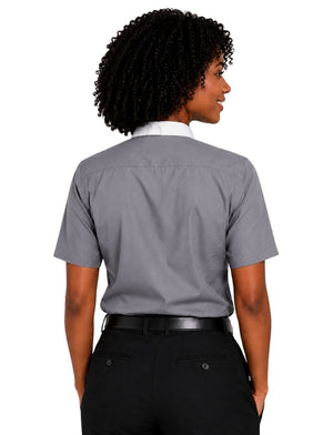 A woman shown from the back wearing a short-sleeve gray clerical shirt tucked into black pants, against a plain white background.