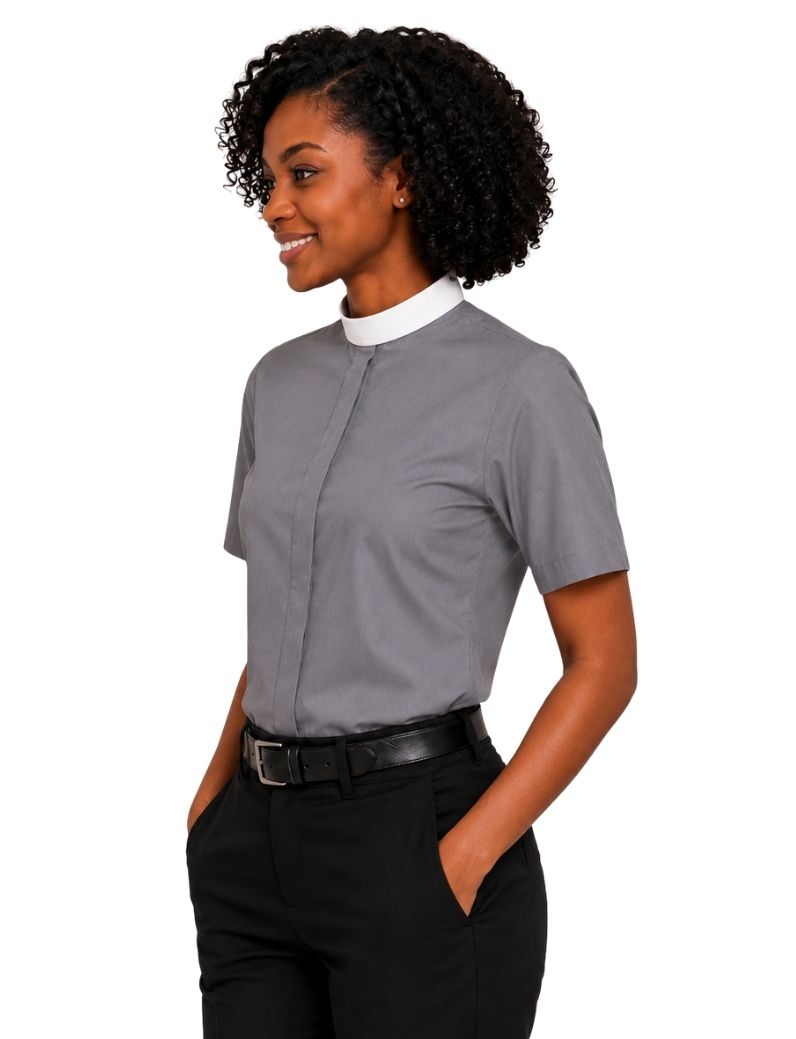 A woman with curly black hair wearing a gray short-sleeve clerical shirt with a white mock neck collar, paired with black pants and a black belt, shown against a plain white background.