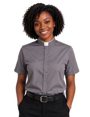 A smiling woman with curly black hair wearing a short-sleeve gray clerical shirt with a white collar, paired with black trousers and a black belt, against a plain white background.