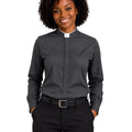 A smiling woman with curly black hair wearing a dark gray long-sleeve clerical shirt with a white collar, paired with black trousers and a black belt, against a plain white background.