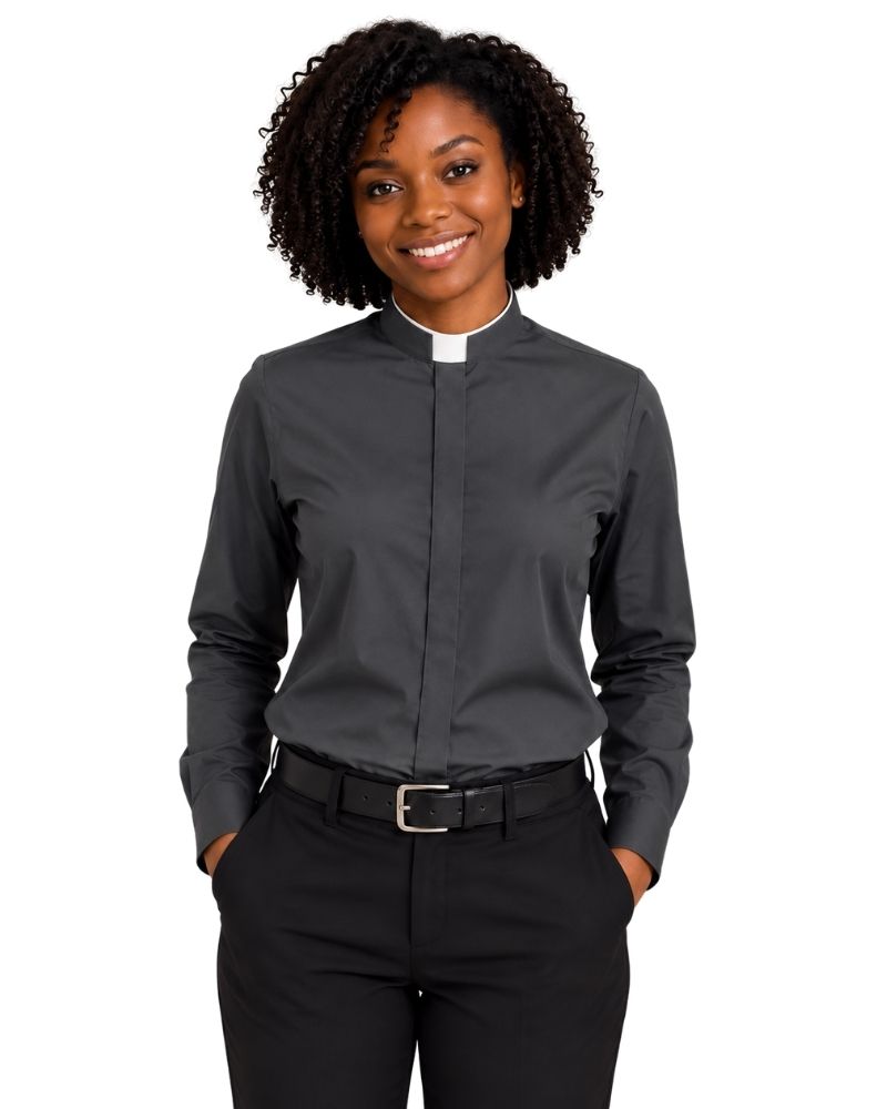 A smiling woman with curly black hair wearing a dark gray long-sleeve clerical shirt with a white collar, paired with black trousers and a black belt, against a plain white background.