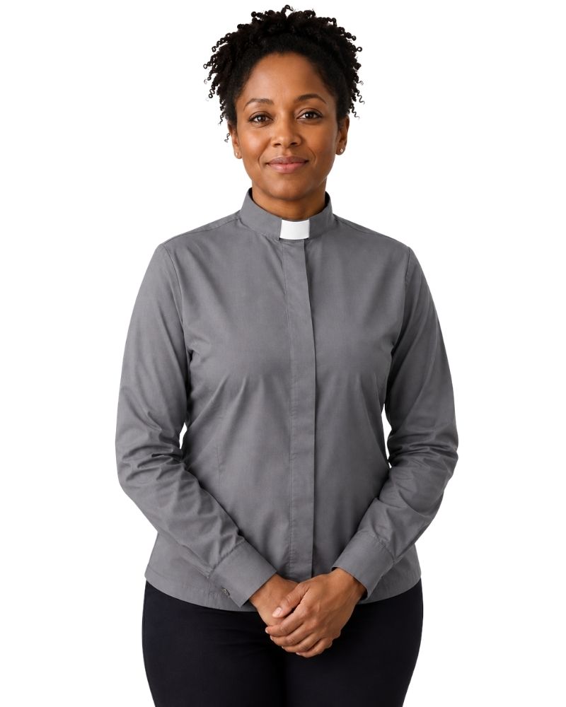 A woman wearing a gray long-sleeve clerical shirt with a white collar tab, paired with black trousers, standing against a plain white background.
