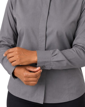 A close-up of a woman wearing a long-sleeve gray clerical shirt, with both hands adjusting the cuff.