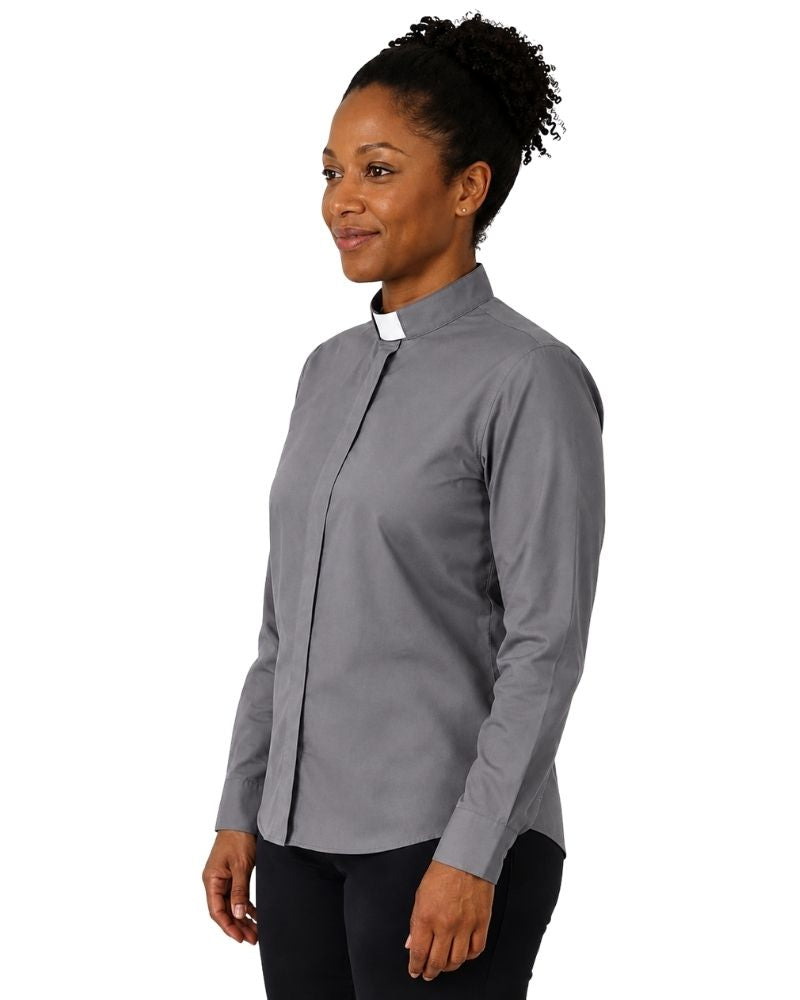A woman wearing a long-sleeve gray clerical shirt with a white collar, standing against a plain white background.