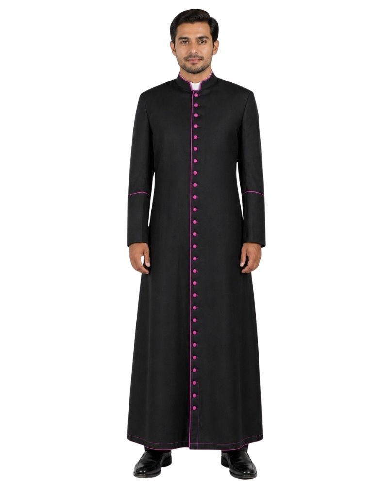 A man modeling a long black traditional Cassock with a high collar, front button closure, and magenta trim details, set against a plain white background.