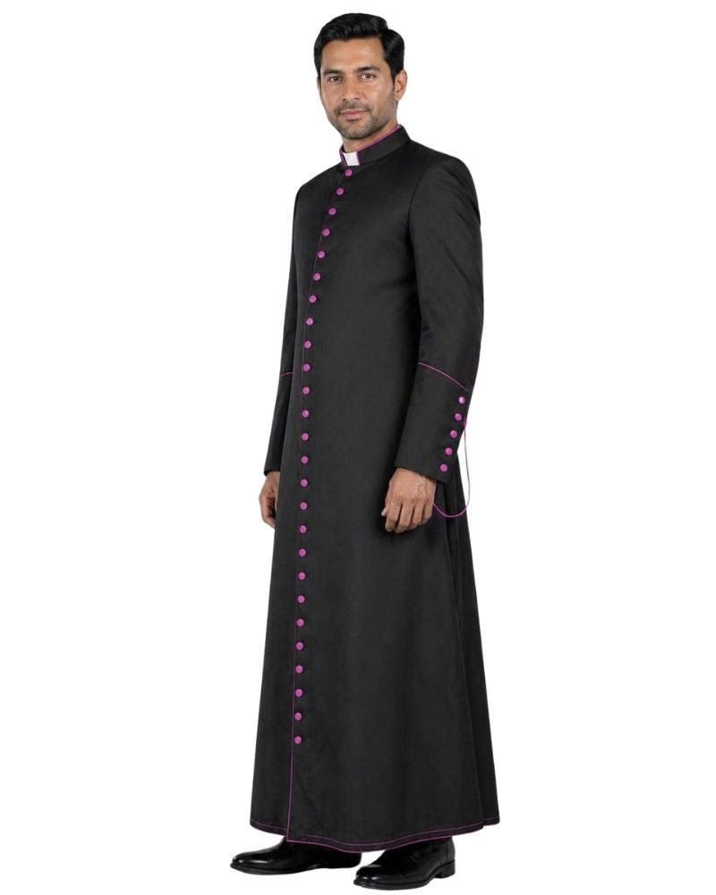A man modeling a long black traditional Cassock with magenta button accents and trim, standing against a plain white background.