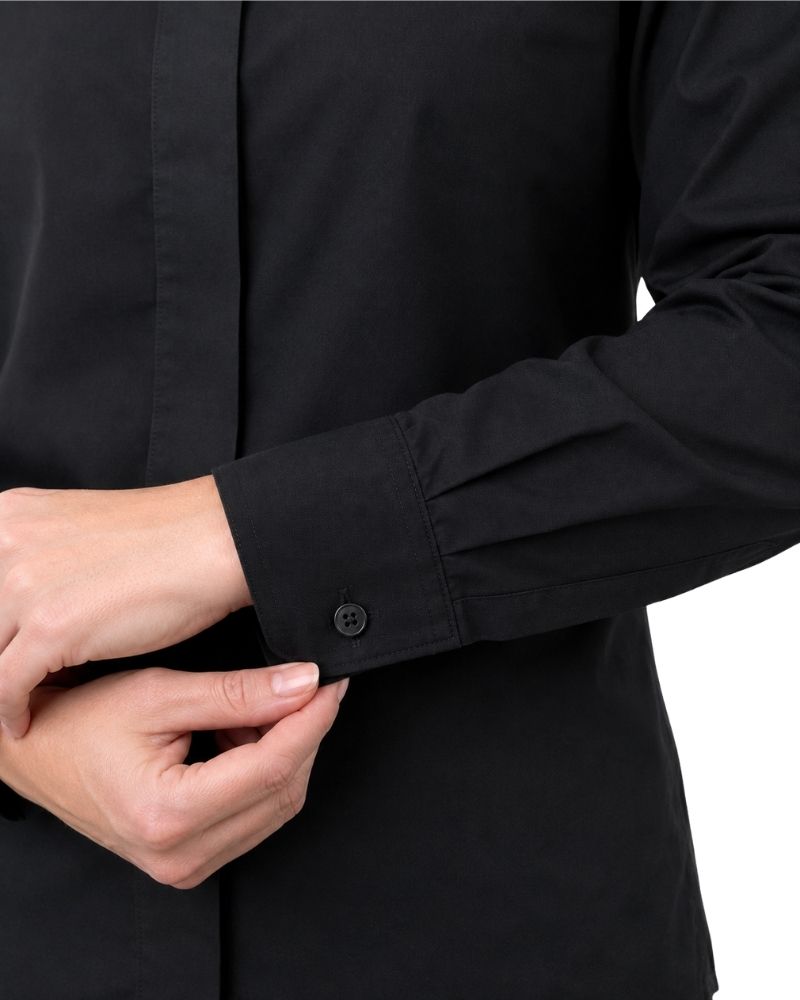 Close-up of a women hands adjusting the cuff of a black long-sleeve button-up shirt, showing the fabric texture and a single black button.