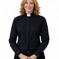 A smiling blonde woman wearing a black long-sleeve clerical shirt with a white collar, standing against a plain white background.